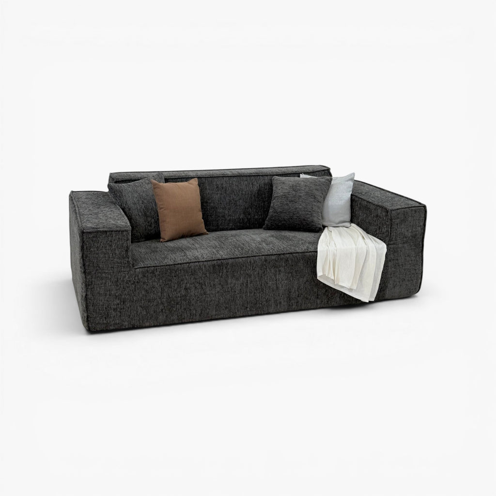 Furnology Blocco Compressed 3 seater sofa in dark grey textured fabric with brown and grey cushions and a white throw.