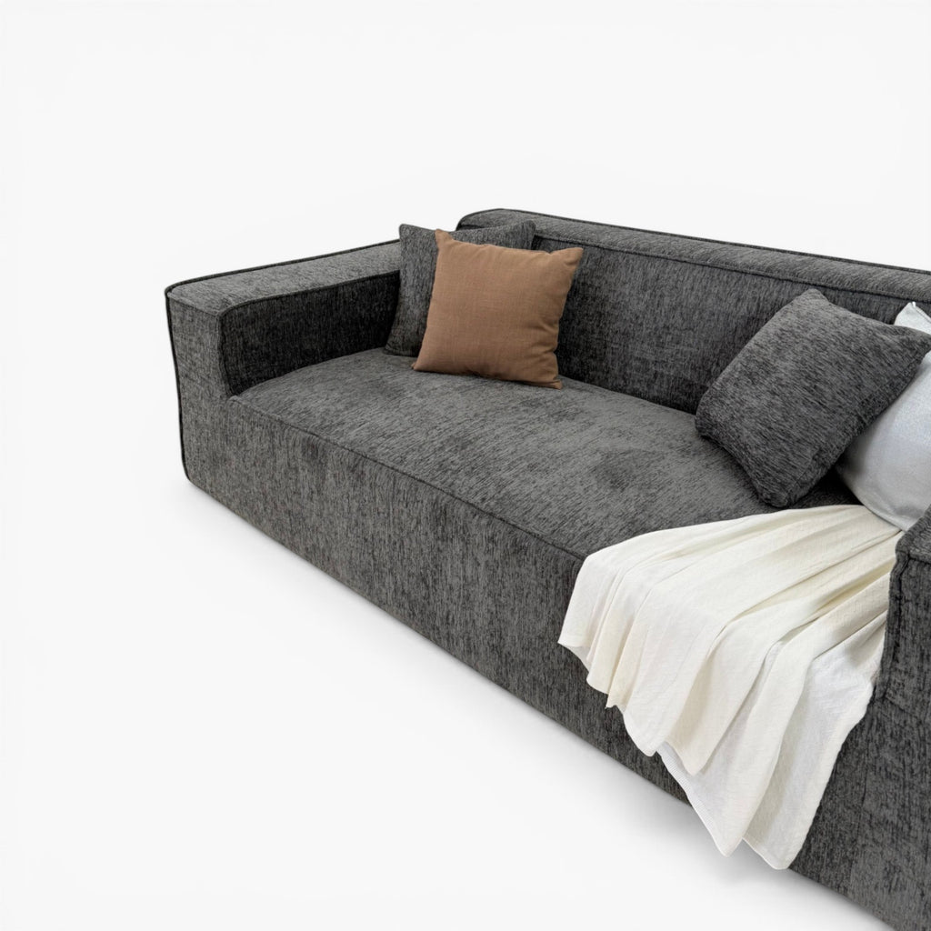 Furnology Blocco Compressed 3 seater sofa in dark grey textured fabric with brown and grey cushions and a white throw.